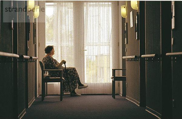 Seitenansicht einer alten Frau sitzend einsam in einem Korridor  Deutschland
