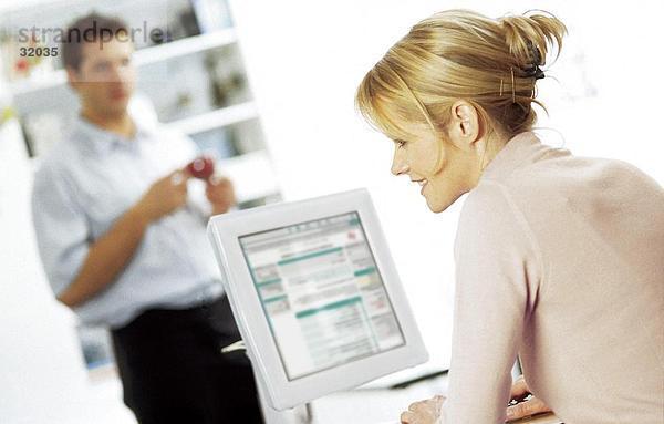 Seitenansicht einer jungen Frau auf einem Computer mit einem jungen Mann stehen im Hintergrund arbeiten