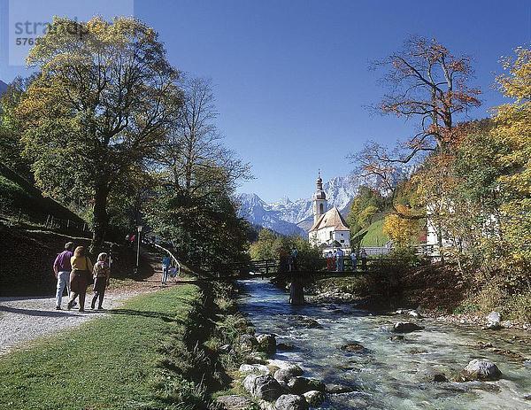 Touristen Wandern am Flussufer mit Kirche im Hintergrund  St.-Sebastian-Kirche  Ramsau Bei Berchtesgaden  Berchtesgadener Land  Bayern  Deutschland