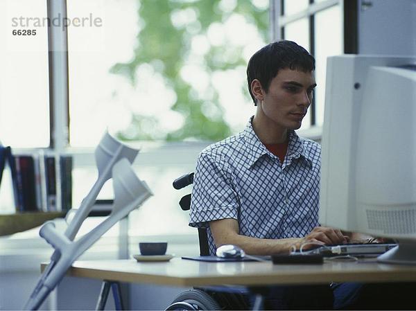 Mann im Rollstuhl mit Computer im Büro