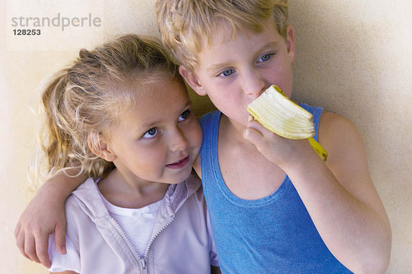 Junge umarmt Schwester und isst Banane