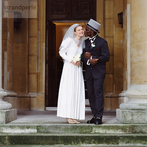 Bräutigam küsst Braut vor der Kirche
