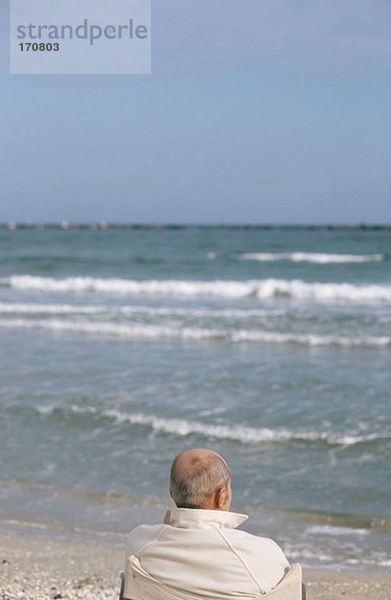 Älterer Mann schaut auf die Wellen