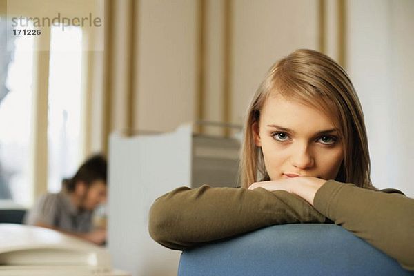 Frau  die sich auf den Rücken ihres Stuhls lehnt.