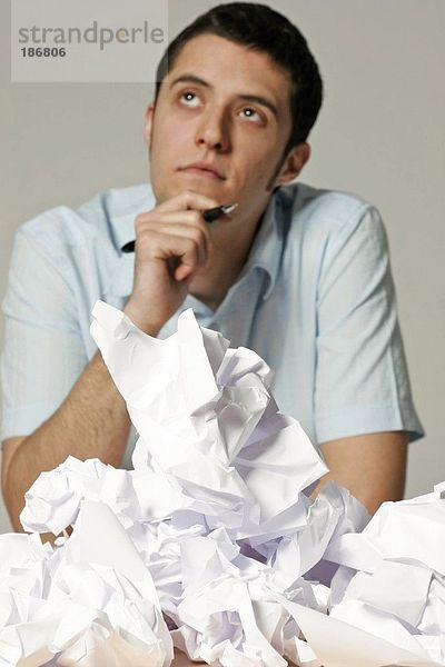 Junger Mann am Schreibtisch sitzend mit zerknittertem Papier