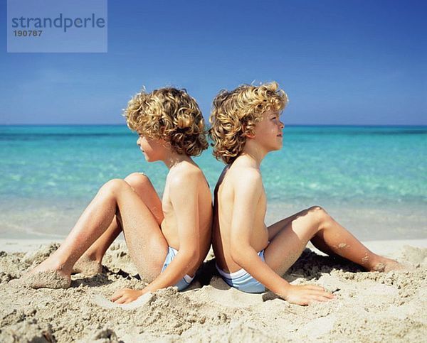 Zwillingsjungen am Strand sitzend