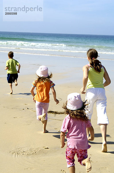 Rückansicht Frau spielen mit ihren drei Kindern am Strand