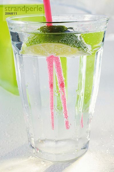 Glas Wasser mit Limettenschnitz und Strohhalm