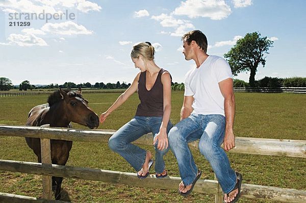 Paar auf einem Zaun sitzend mit Pferd