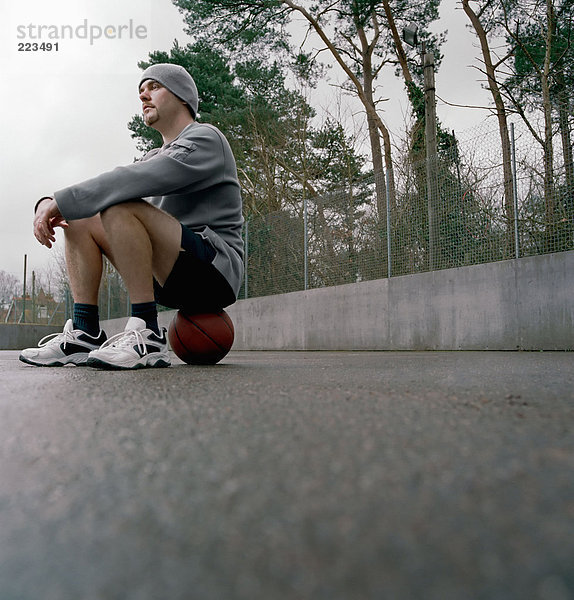 Junger Mann auf einem Basketball sitzend