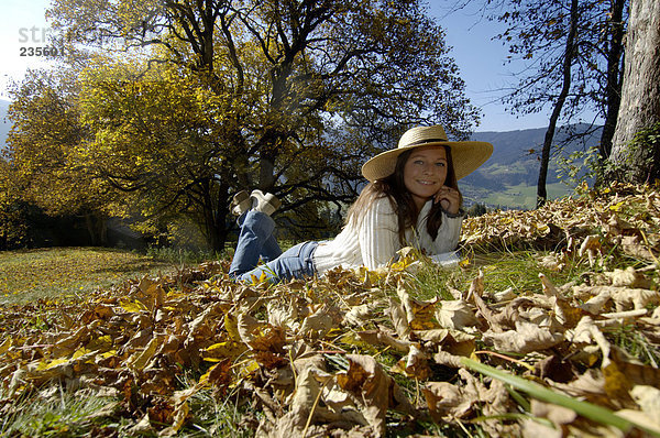 Junge Frau auf Herbstlaub liegend mit Hand am Kinn  Portrait