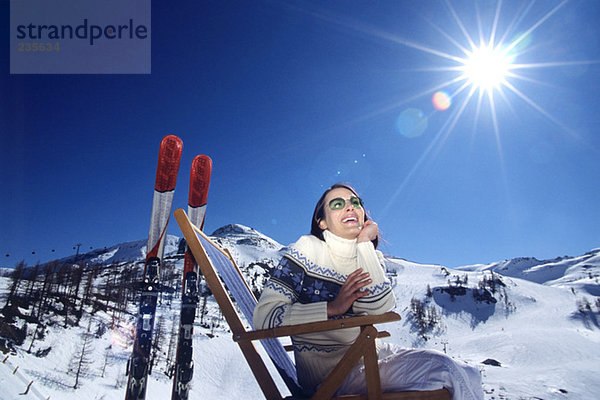 Österreich  Frau sitzt auf Liegestuhl in den Schneealpen  lächelnd  Blickwinkel niedrig