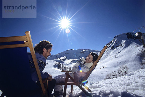 Junges Paar auf Liegestühlen in den Alpen sitzend  lächelnd