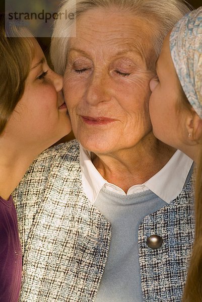 Zwei Mädchen (8-11) küssen Großmutter  Nahaufnahme