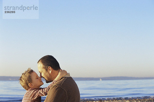 Vater und Sohn (6-9) von Angesicht zu Angesicht am Strand  Seitenansicht