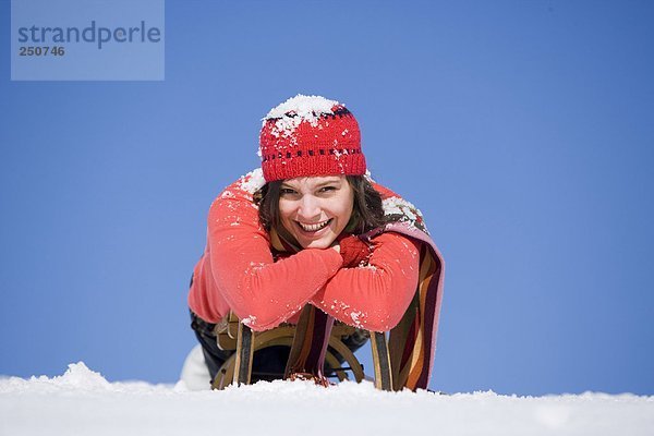 Frau mit Schnee bedeckt auf Schlitten liegend  lächelnd