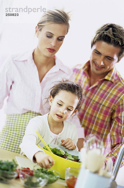 Eltern beobachten Tochter (6-7) bei der Zubereitung von Salat