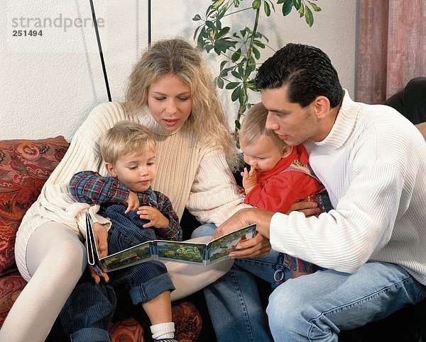 10229175  Bild  Buch  Eltern  Familie  zusammen  lesen  Sofa  Wohnzimmer  zwei  Kleinkinder  Kinder