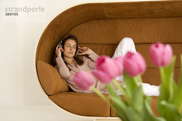 Frau entspannt auf Sofa mit Kopfhörern  rosa Tulpen im Vordergrund
