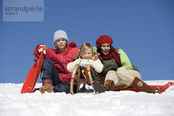Österreich  Mädchen (6-17) sitzend mit Schlitten im Schnee  lächelnd  Portrait