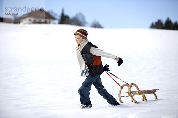 Österreich  Junge (12-13) zieht Schlitten im Schnee  Seitenansicht