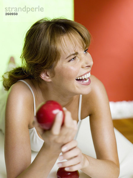 Frau auf dem Bett liegend  Apfel haltend  lachend  Nahaufnahme