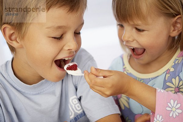 Mädchen steckt Jungen Löffel mit Joghurt in Mund
