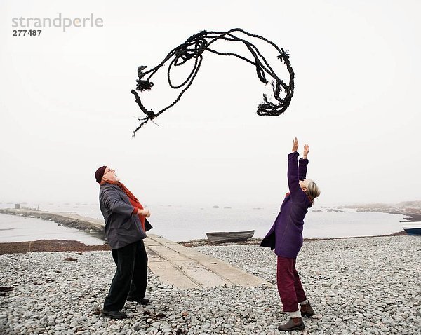 Ein Mann und eine Frau werfen ein Seil an einem Strand.