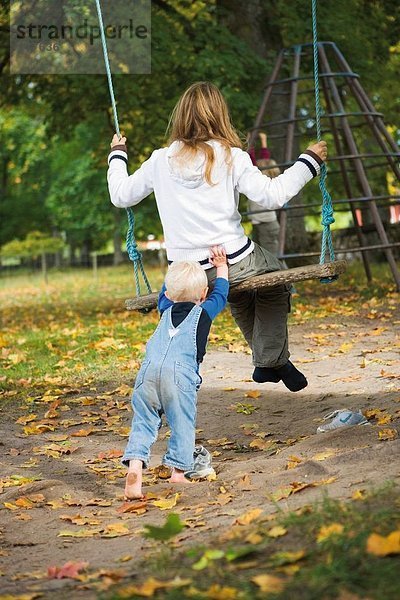 Kleines Mädchen drücken ihre Schwester auf eine Schaukel.