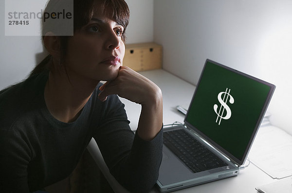 Frau tagträumt mit Dollarzeichen auf ihrem Laptop