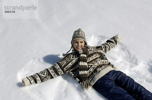 Junge Frau auf Schnee liegend  lächelnd  Portrait