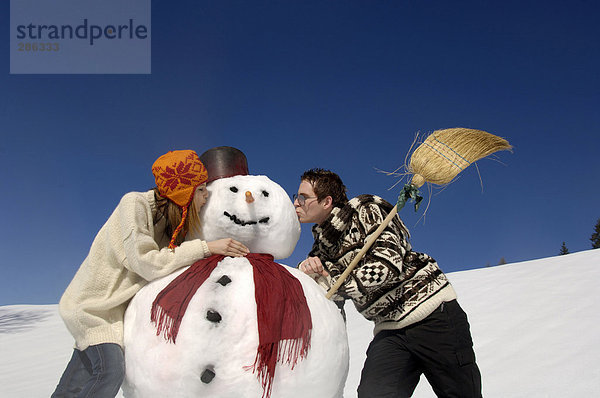 Junges Paar küsst Schneemann  Blick in den tiefen Winkel