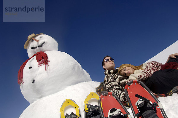 Junges Paar auf Schneemann gelehnt mit Schneeschuhen  Tiefblick