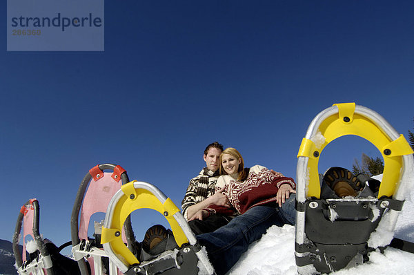 Junges Paar im Schnee sitzend mit Schneeschuhen  Tiefblick