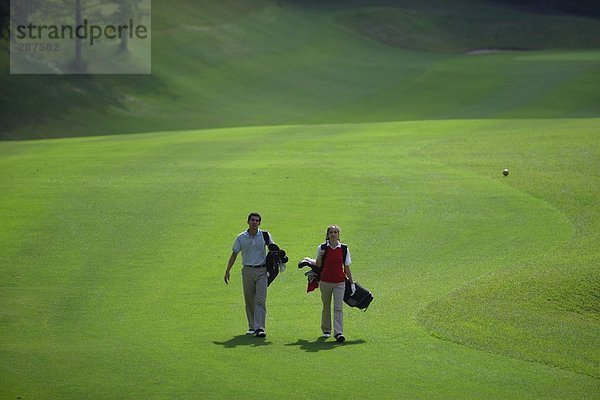 Paar zu Fuß auf dem Fairway trägt ihre Golfbeutel