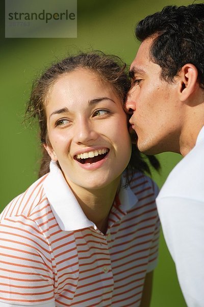 Junge weibliche Golfer wird von jungen Mann auf die Wange geküßt