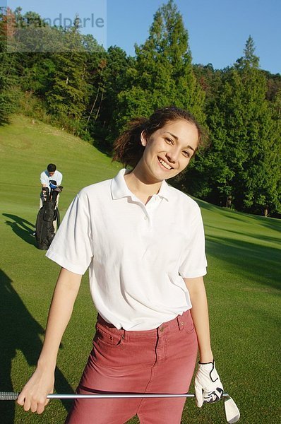 Weibliche Golfer Lächeln in die Kamera mit einem Mann im Hintergrund