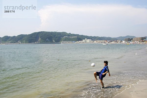 Junger Mann spielen Fußball am Strand