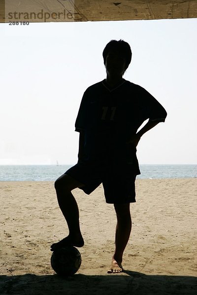 Silhouette eines jungen Mannes mit einem Fußball am Strand