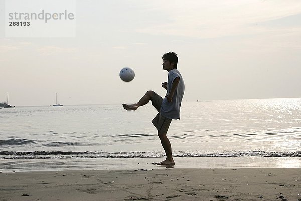 Junger Mann spielen Fußball am Strand