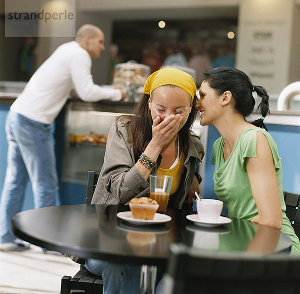 Zwei Frauen in einem Café lachen.