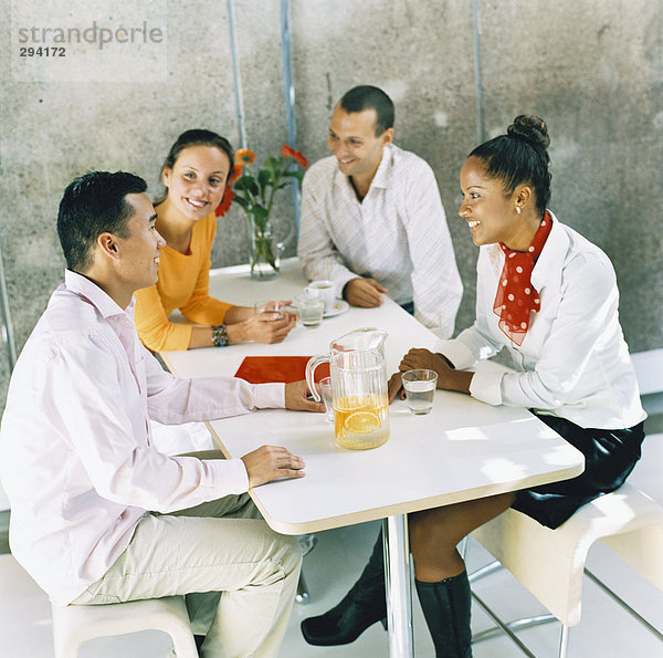 Zwei Männer und zwei Frauen sitzen von einer Tabelle mit Erfrischungen.