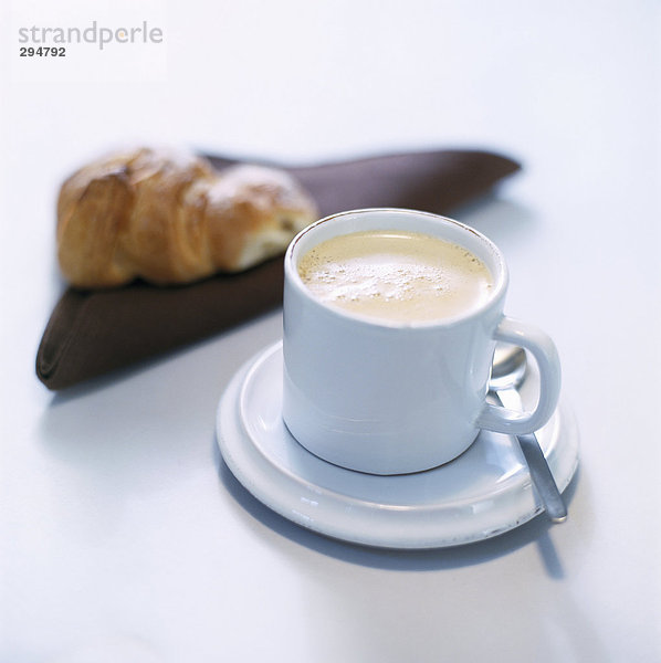 Eine Tasse Kaffee und einem Croissant im Hintergrund.