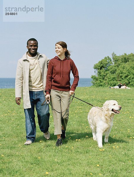 Ein lächelnd paar zu Fuß mit einen Hund.