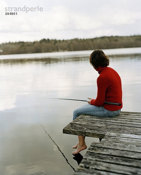 Eine Frau auf einer Brücke Fischerei Rückansicht sitzend.