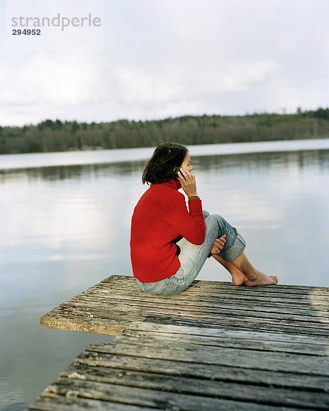 Eine Frau auf einer Brücke redend über ein Mobiltelefon Rückansicht sitzend.