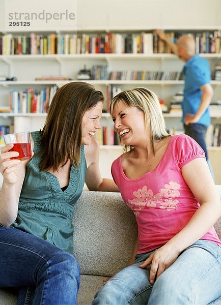 Zwei Frauen in einem Sofa lachen.