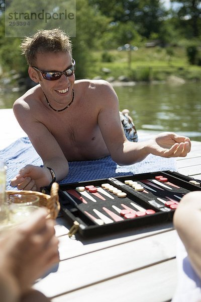 Ein Mann in Sonnenbrillen liegend auf einer Brücke spielen Backgammon.