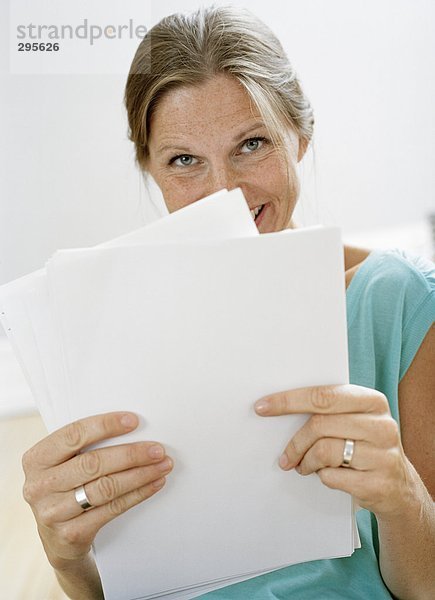 Einer blonden Frau hält Papiere an ihr Gesicht.
