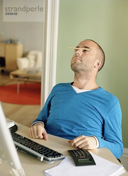Ein Mann Netzwerklastenausgleich einen Bleistift auf seine Nase in einem Büro.